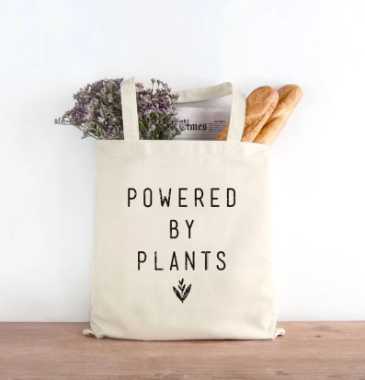 wooden surface with a vegan tote bag that says "powered by plants"