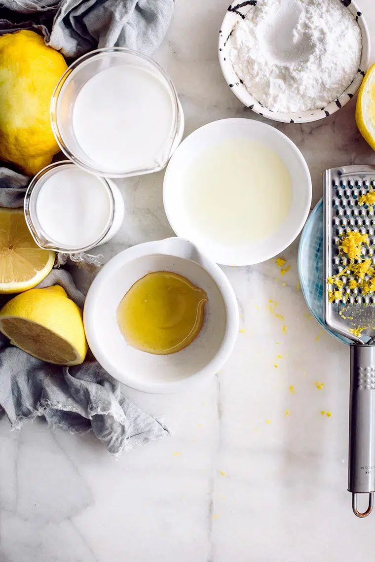 white table with some lemons and several small bowls containing plant based milk, sweetener and vanilla