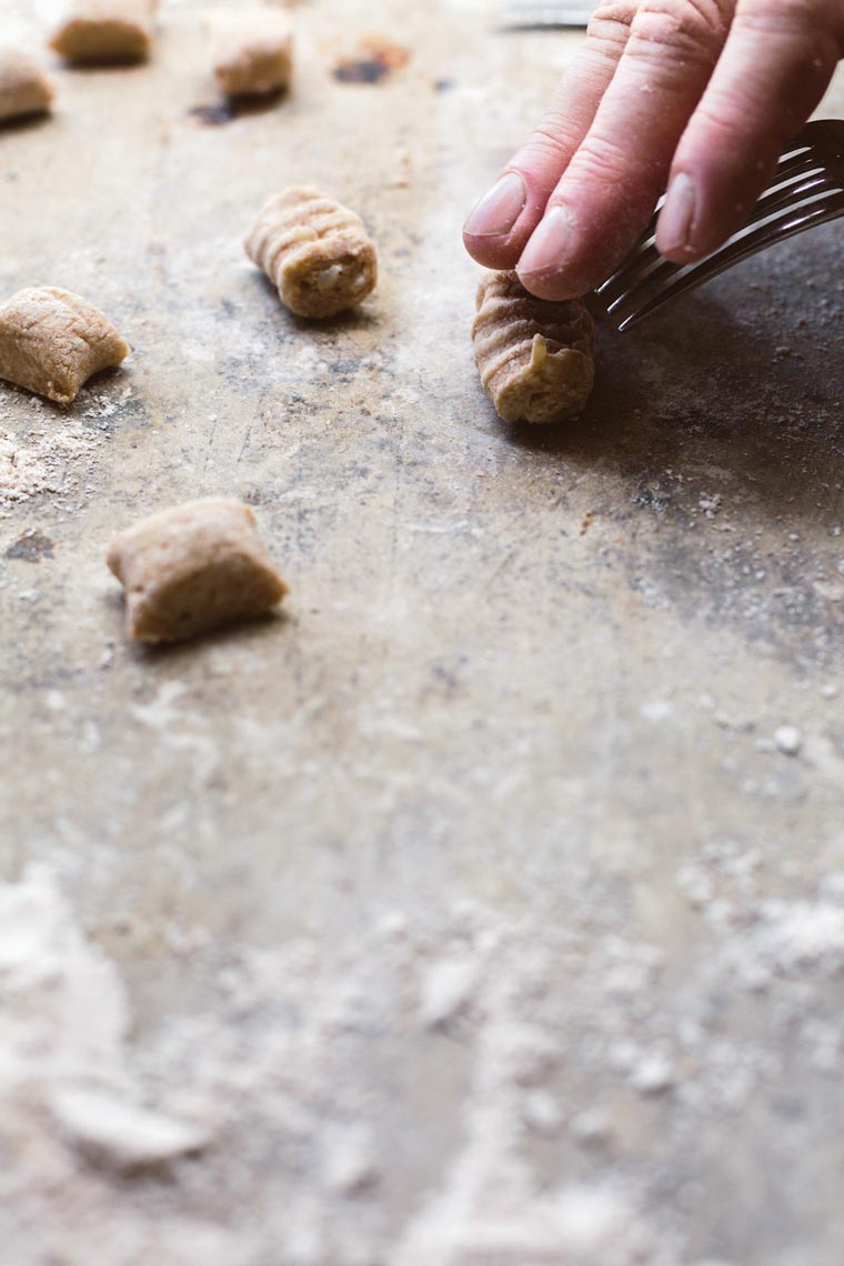 close up of a hand with a fork that creates the traditional shapes in the uncooked whole wheat gnocchi