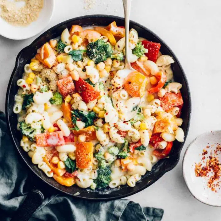 white table with a large black pan containing colorful vegetables, pasta and vegan white sauce