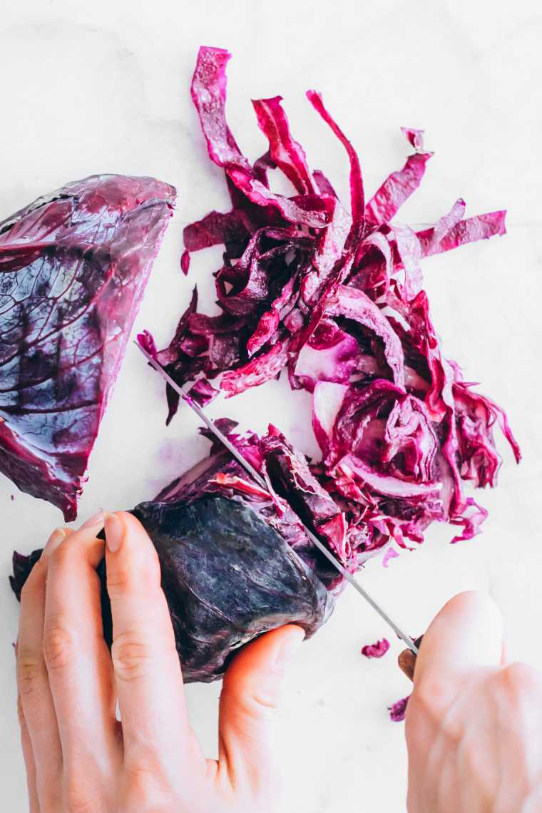 two hands cutting red cabbage on a white surface