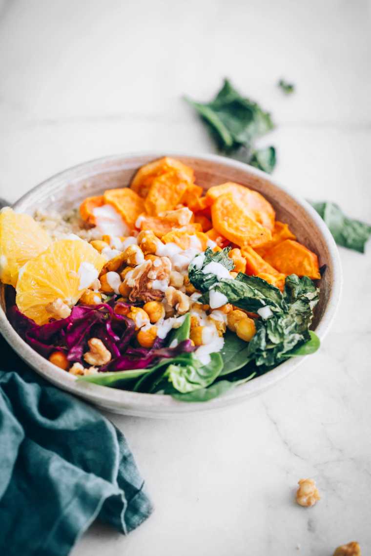 white table with a rainbow Buddha bowl consisting of sweet potato, kale, spinach, red cabbage, orange and chickpeas