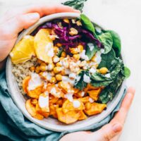 two hands holding a colorful vegan rainbow bowl over a table