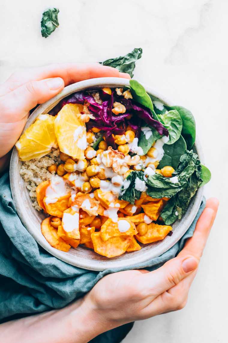 two hands holding a colorful vegan rainbow bowl over a table