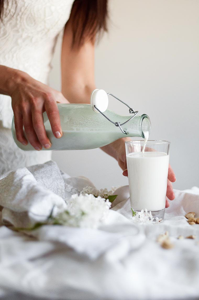 Woman pouring homemade cashew milk from bottle into a glass