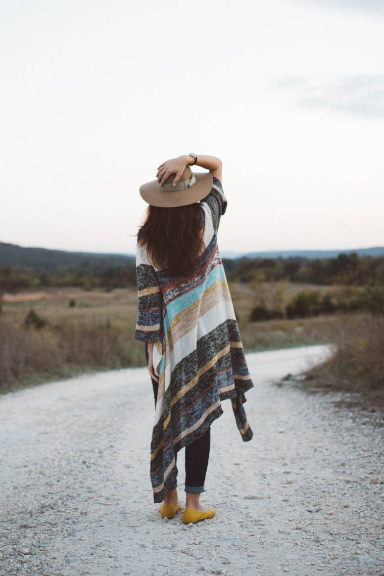woman with a hat and large cardigan standing on a road