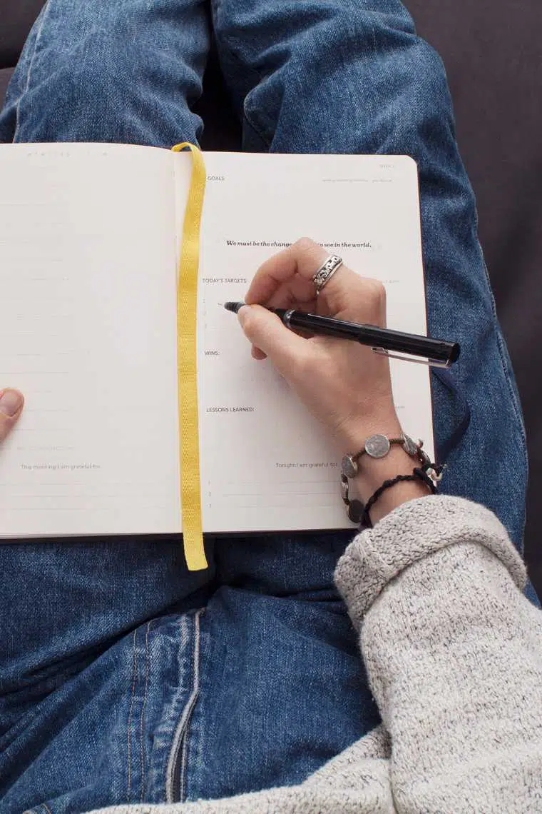 Top view of woman with blue jeans and bracelets writing in her journal