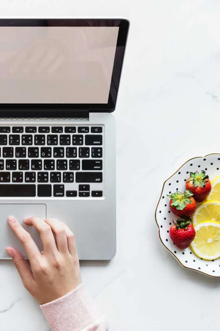Woman hand using trackpad of laptop with plate of strawberries and lemons next to her
