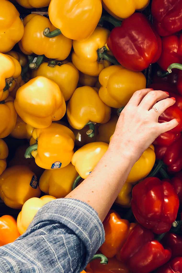 Woman in supermarket reaching for a bell pepper
