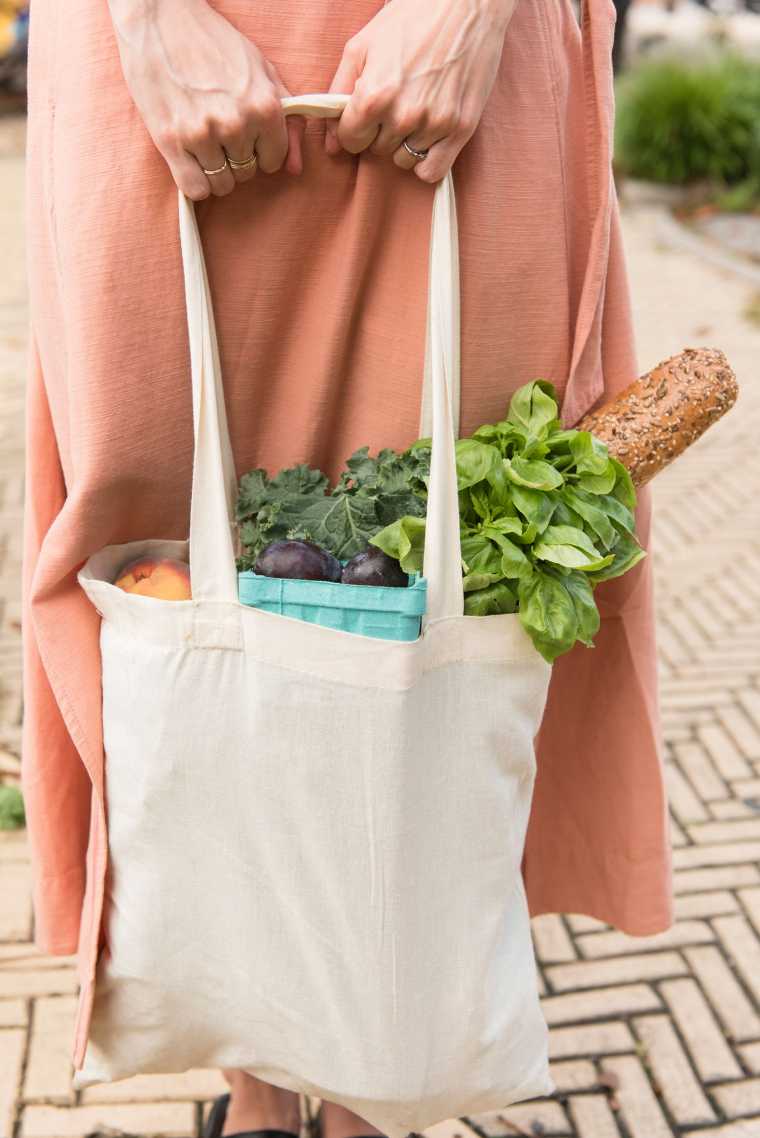 woman in dress standing on the street with a bad of vegan groceries in her hand