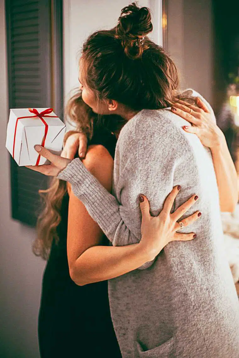 Two women hugging each other, one of them with Christmas gift in her hand