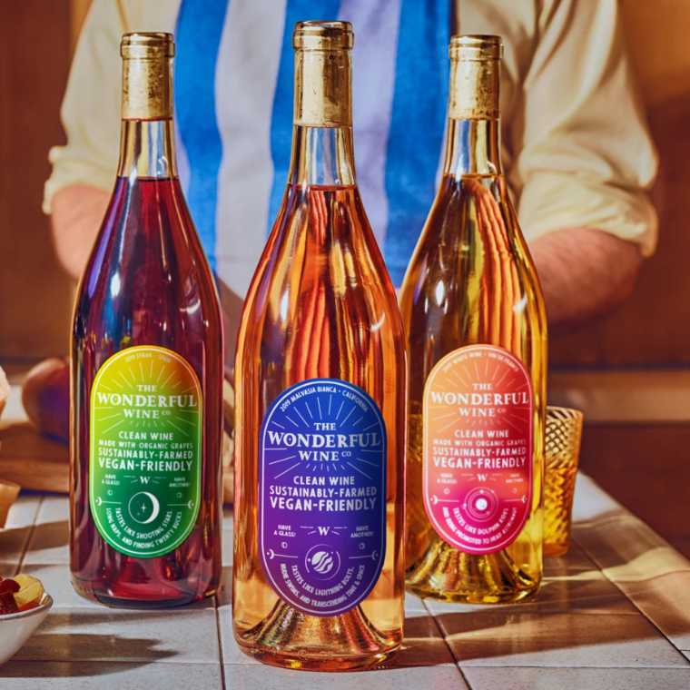table with three bottles of colorful vegan wine and a man behind them
