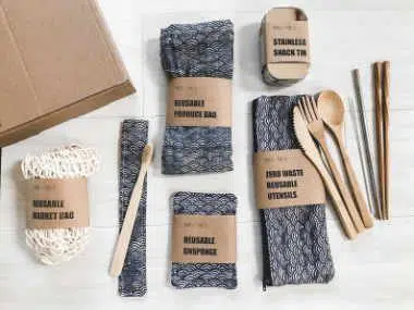 set of bamboo cutlery, reusable bags, straws and snack tin next to a carton