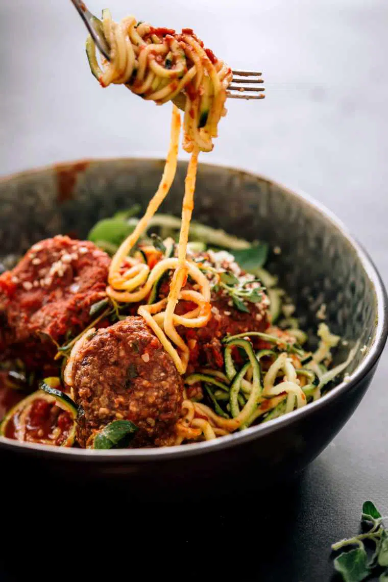 Closeup of zoodles with marinana and black bean meat balls with some zucchini noodles rolled round a fork