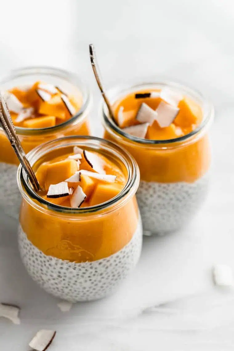 four small glass jars with coconut chia pudding that's topped with mango puree