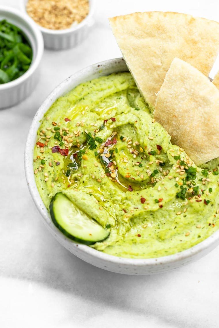 white bowl with vibrantly green edamame hummus and some chips on a table