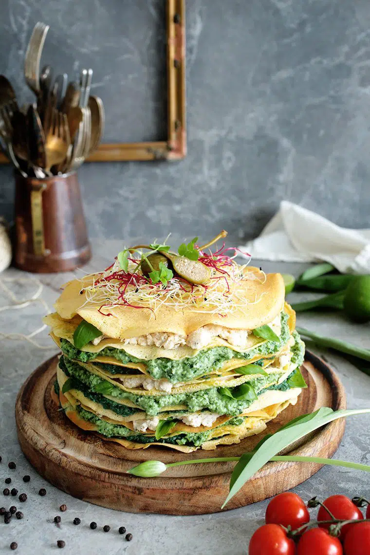 wooden cutting board with a layered savory crepe cake and sprouts