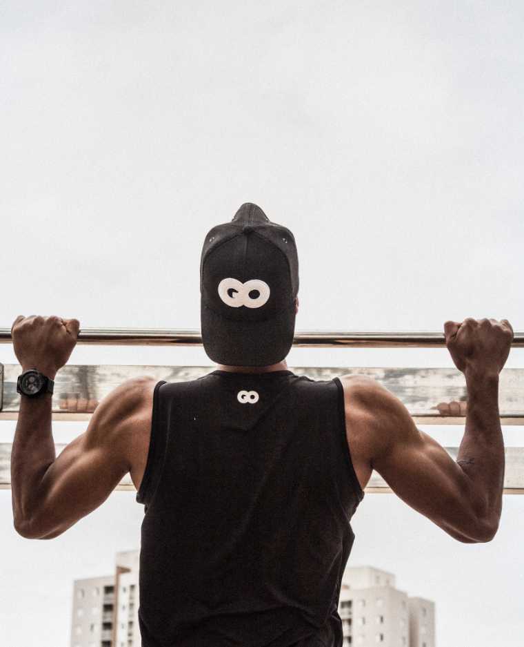 man with black muscle shirt and hat doing pull ups