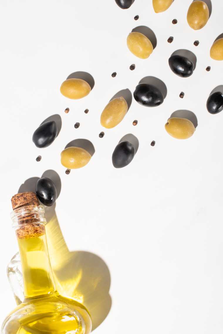 white table with several olives and a bottle of olive oil
