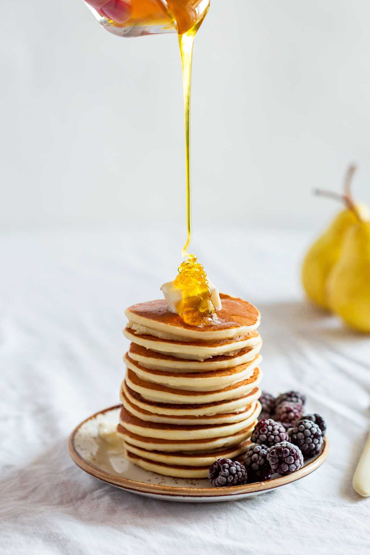 pouring honey over pancakes stacked on a plate