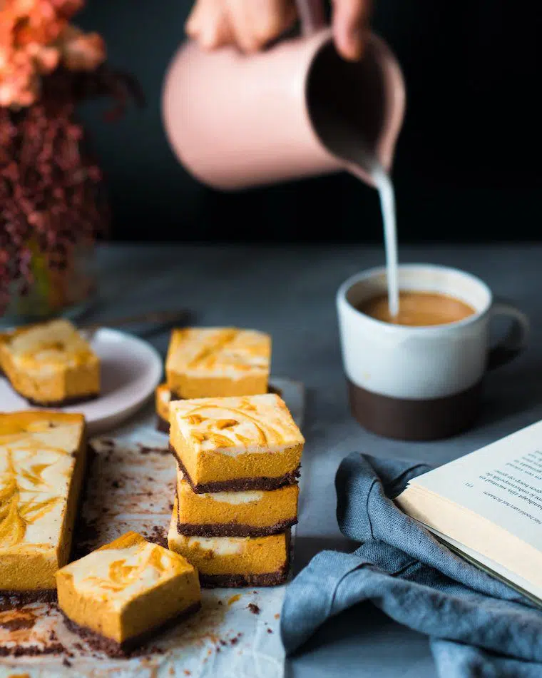 seven pieces of squared bright orange pumpkin cheesecake bars on a table next to a cook and a cup of coffee