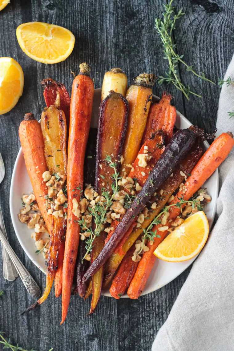 white plate on a wooden table with colorful roasted carrot and nuts