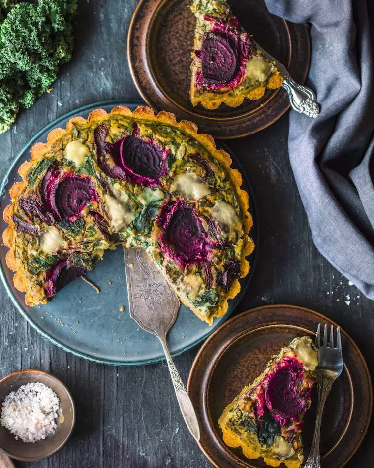 green plate with colorful vegan pumpkin spinach quiche featuring slices of red beets and two plates next to it