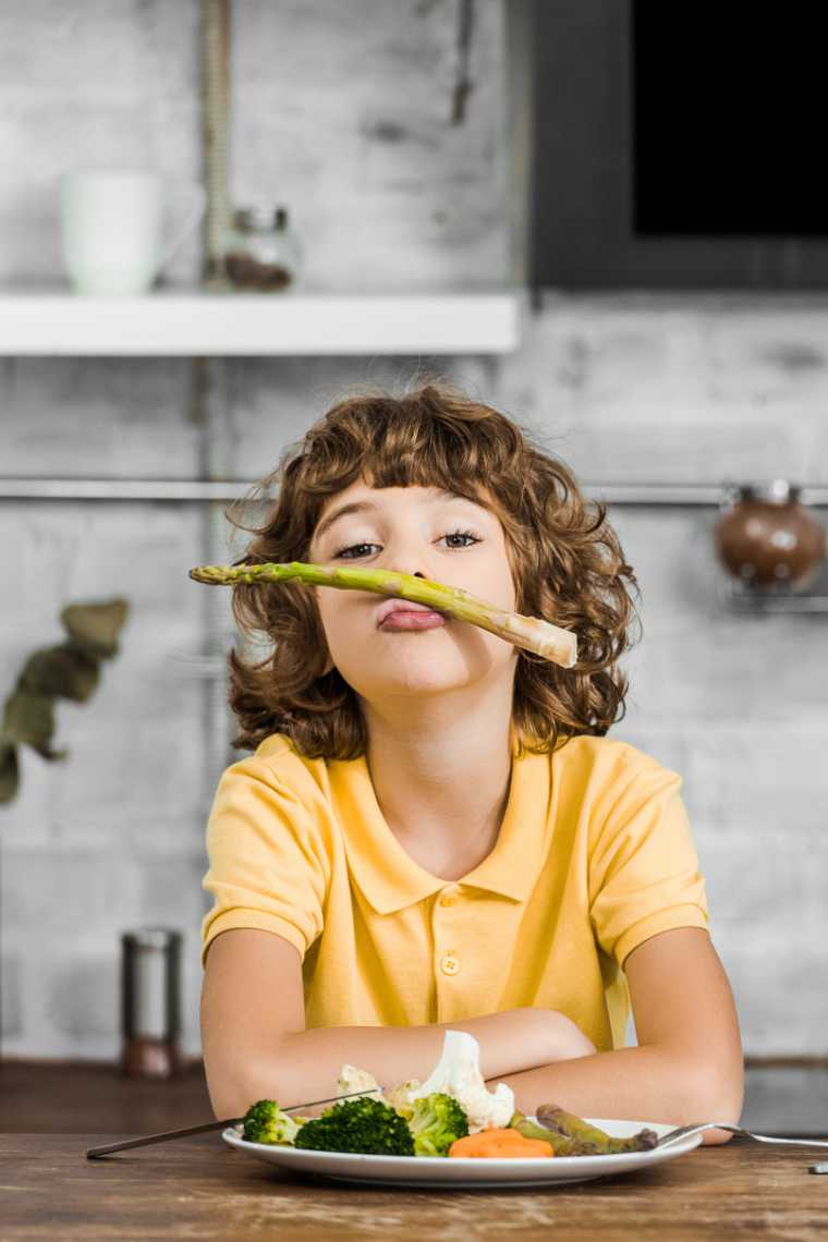young boy in yellow shirt sitting at a table and playing with veggies